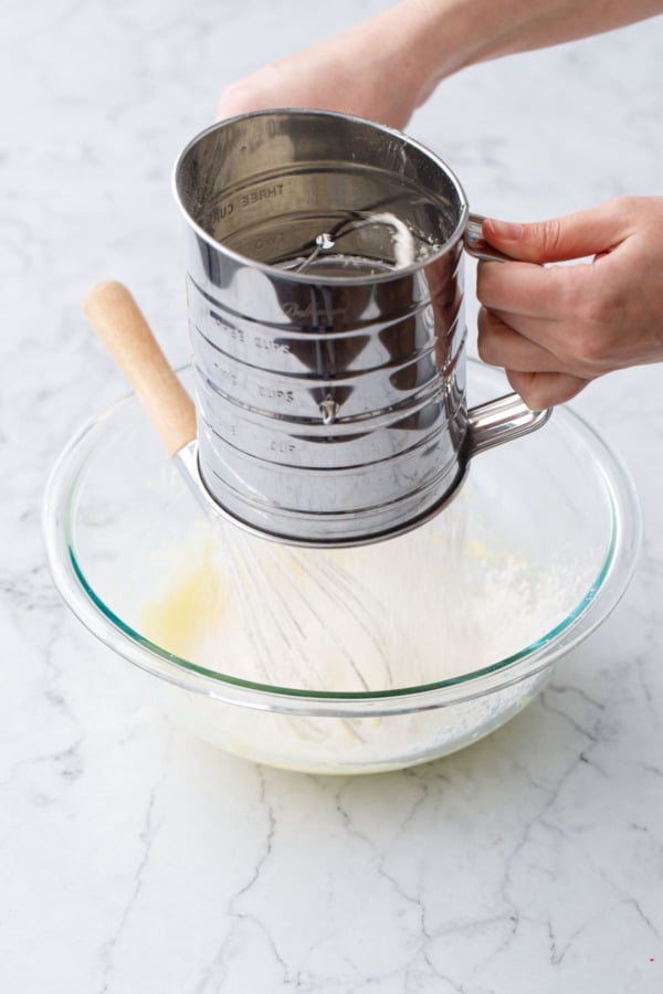Sifting flour and cornstarch over mixing bowl holding the wet ingredients.