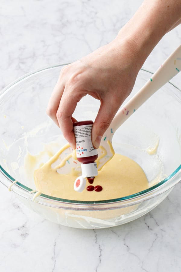 Adding 3 drops of red food coloring to a mixing bowl with uncolored batter.