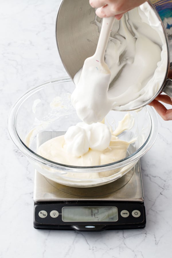 Measuring whipped egg whites into a mixing bowl on a scale.