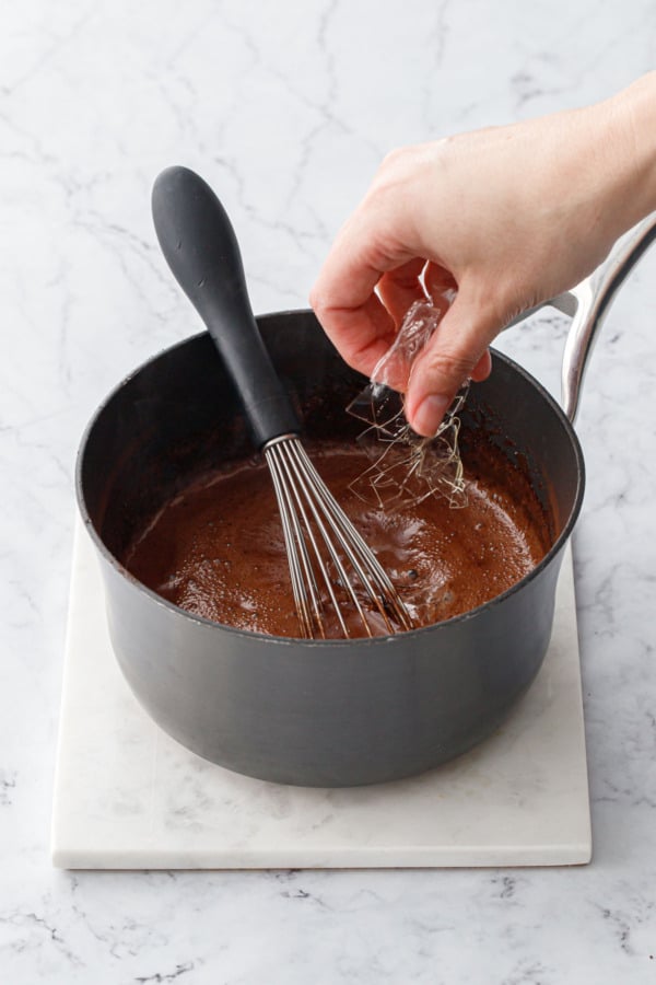 Adding softened leaf gelatin to saucepan with hot cream/cocoa mixture and a whisk on the side.