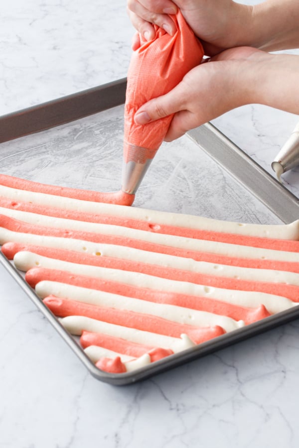 Piping alternating stripes of red and white batter diagonally across a jelly roll pan lined with parchment-paper.