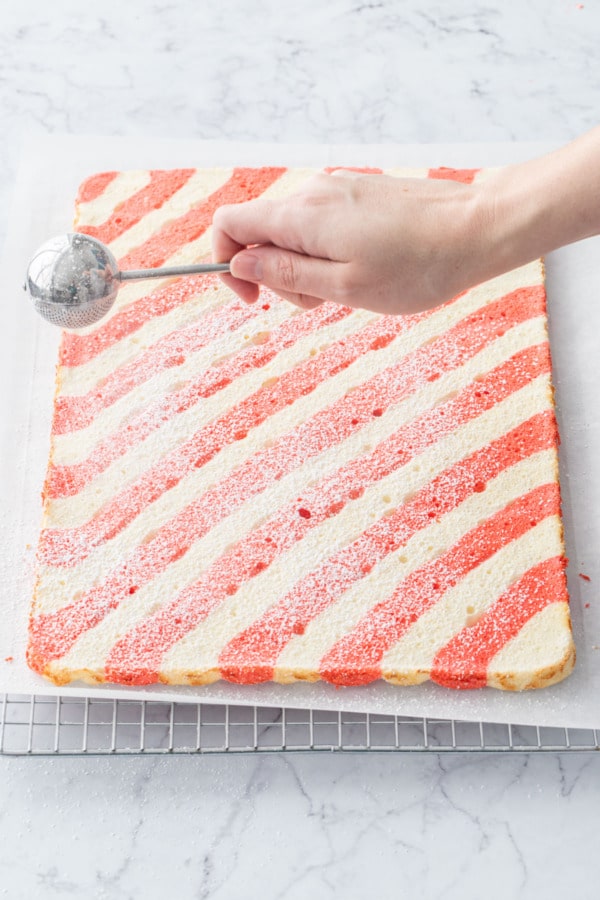 Dusting top of striped cake roll with powdered sugar.