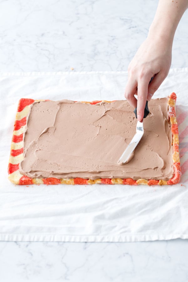 Offset spatula spreading an even layer of filling over the entire cake, with the very edges left empty.