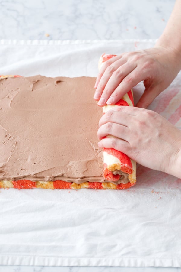 Rolling up the striped cake roll with chocolate whipped cream filling inside.