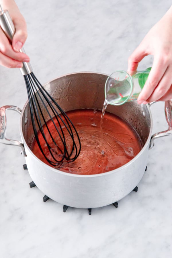 Pouring citric acid dissolved in water into saucepan with leftover orange sugar syrup.