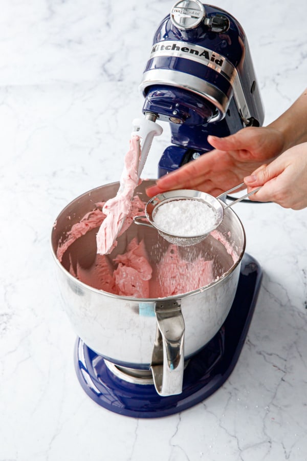 Sifting powdered sugar into mixing bowl of stand mixer.