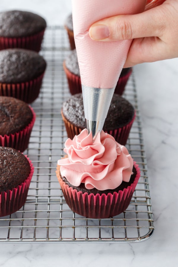 Piping a swirl of light pink blood orange buttercream on top of a chocolate cupcake.