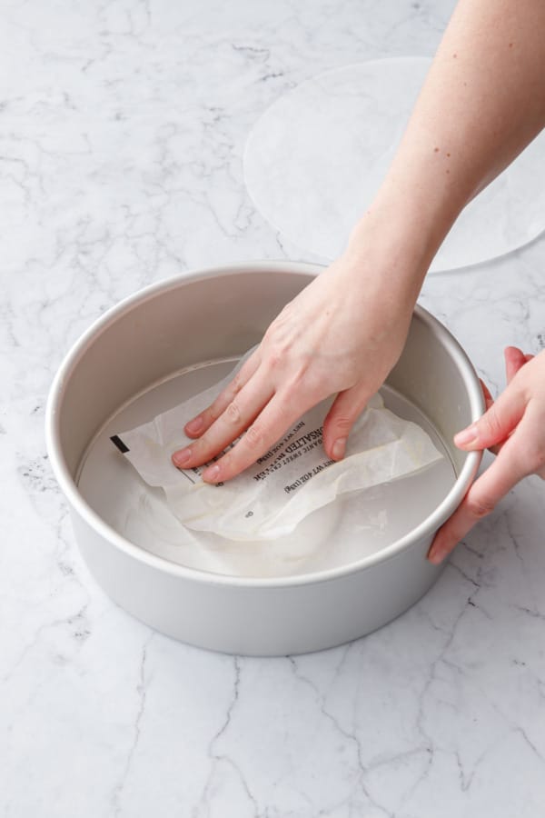 Using a butter wrapper to grease the inside of a 9-inch aluminum cake pan with removable bottom.