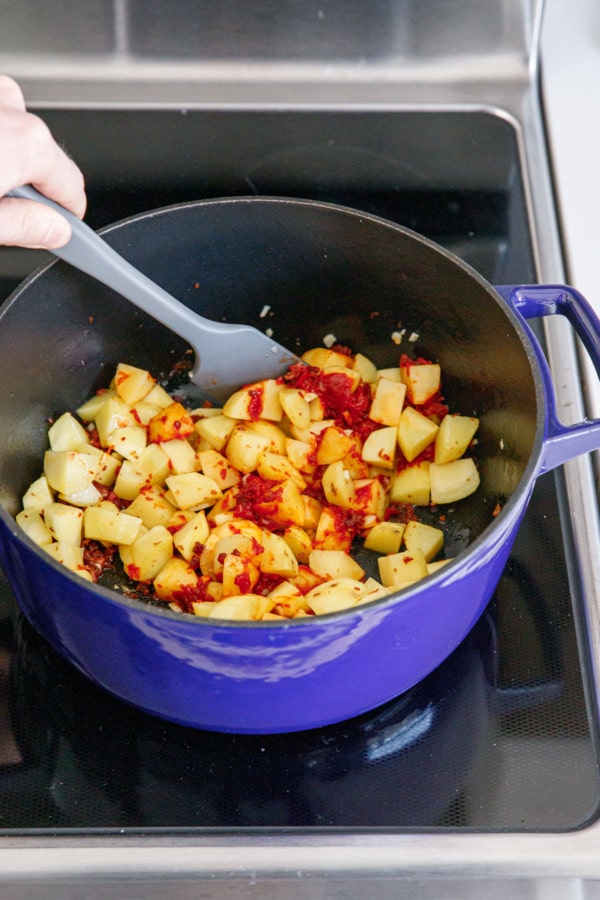 Stirring tomato paste into a Dutch oven on the stovetop with potatoes and pancetta.