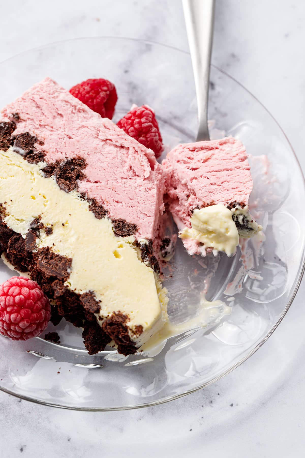 Closeup, slice of Raspberry & Passionfruit Semifreddo with Chocolate Crumbs on a glass plate with a forkful taken out of it.