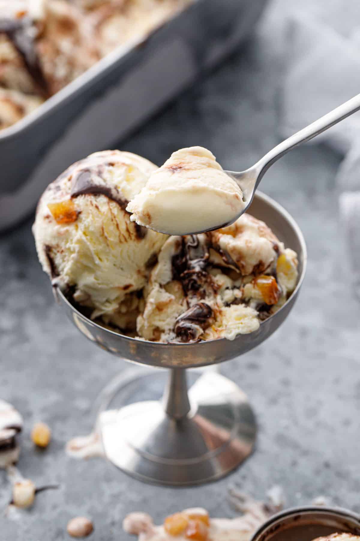 Spooning a scoop of Candied Orange Ice Cream, with a visible fudge swirl and bits of candied orange throughout.