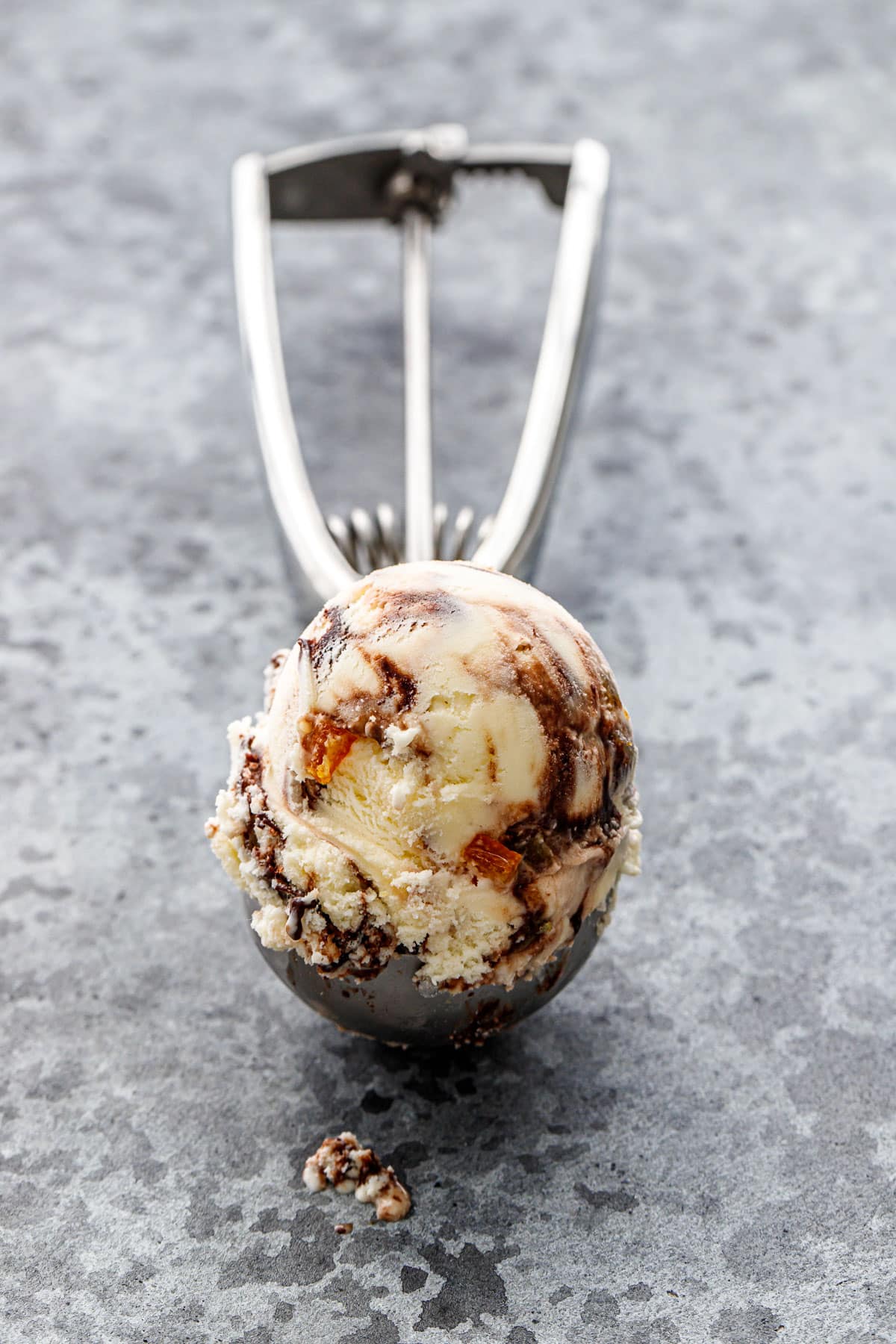 Ice cream scoop with perfect round scoop of Candied Orange Ice Cream with a visible Chocolate Fudge Swirl and bits of candied orange peel throughout.