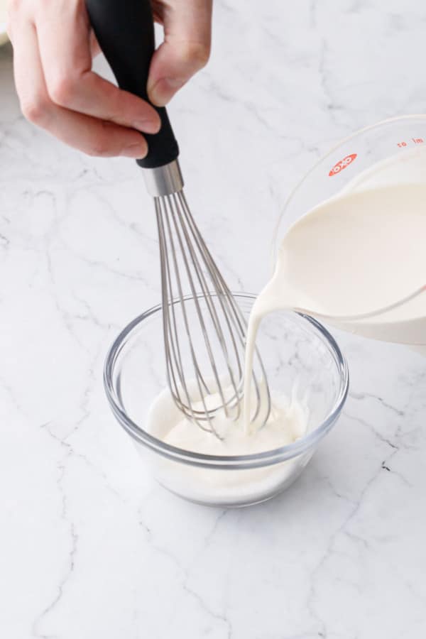Pouring heavy cream into custard cup with sugar and guar gum.
