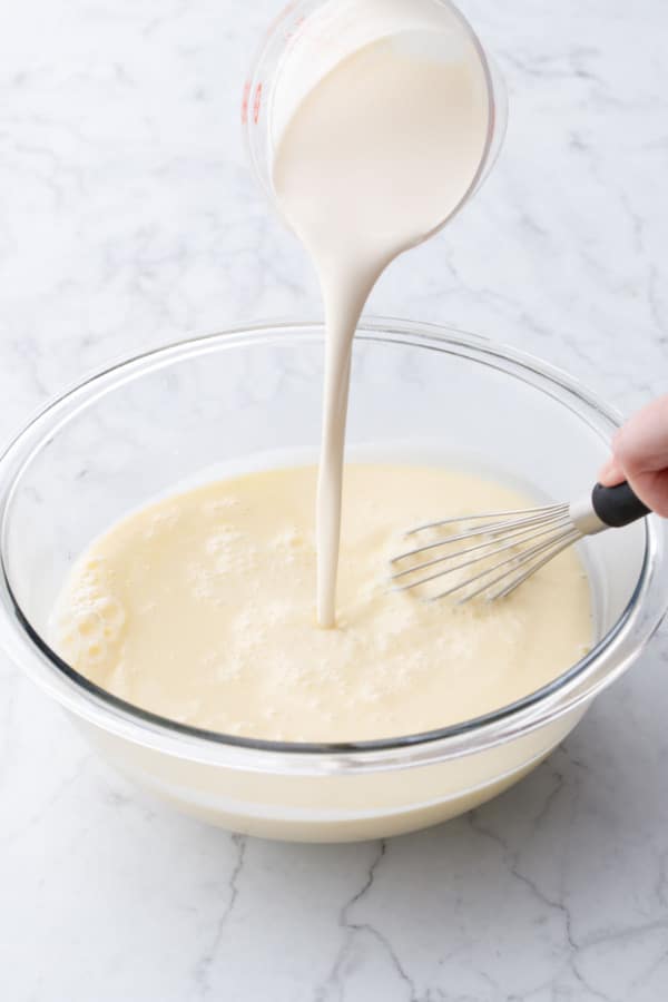 Pouring in cold heavy cream into ice cream base in a glass mixing bowl.