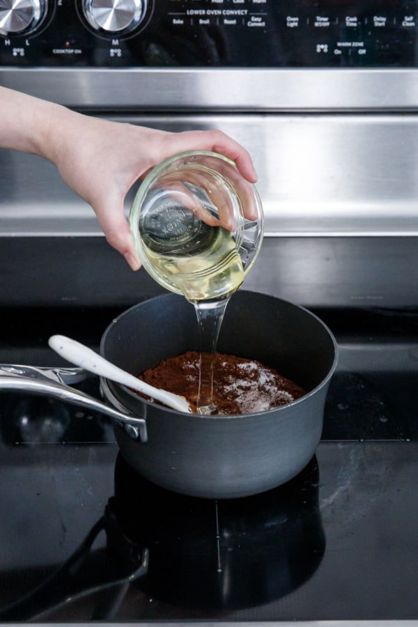 Pouring corn syrup into a small saucepan with cream, sugar, and cocoa powder.