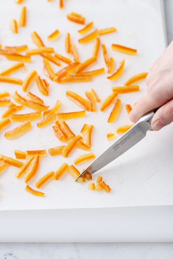 Knife cutting strips of candied orange peel into smaller bits.