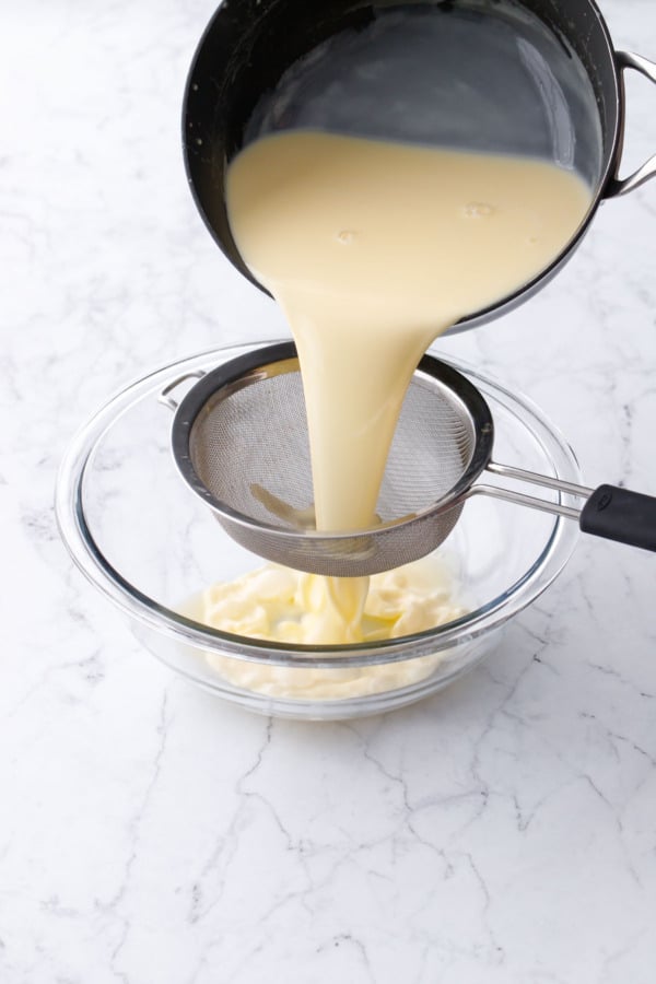 Pouring cooked custard ice cream base through a fine mesh sieve into a bowl.