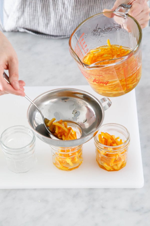 Spooning candied orange peel into sterilized glass canning jars.