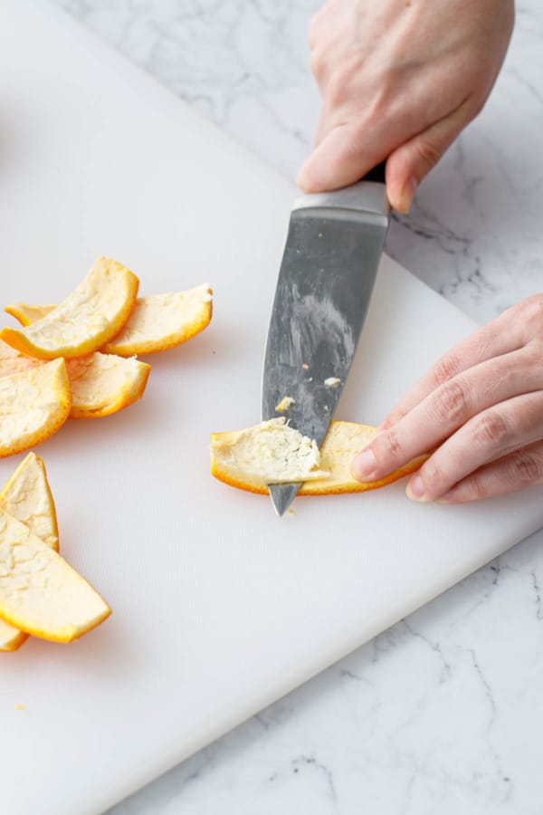 Filleting the excess rind off of the wedges of orange peel.