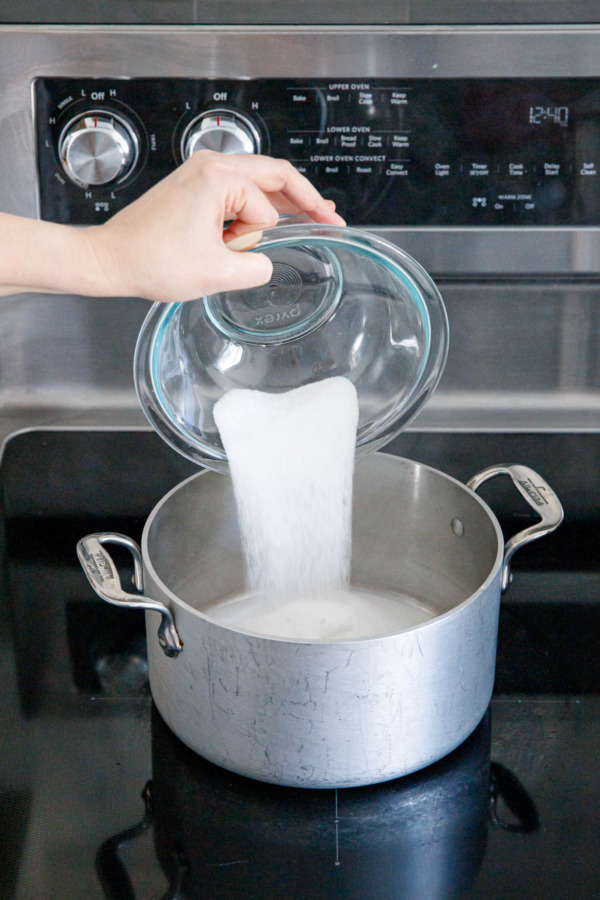 Pouring sugar into a stainless steel saucepan on a glass cooktop.