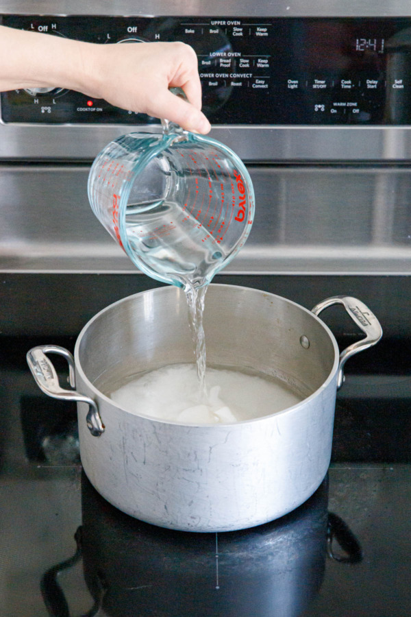 Pouring water into a stainless saucepan along with granulated sugar.