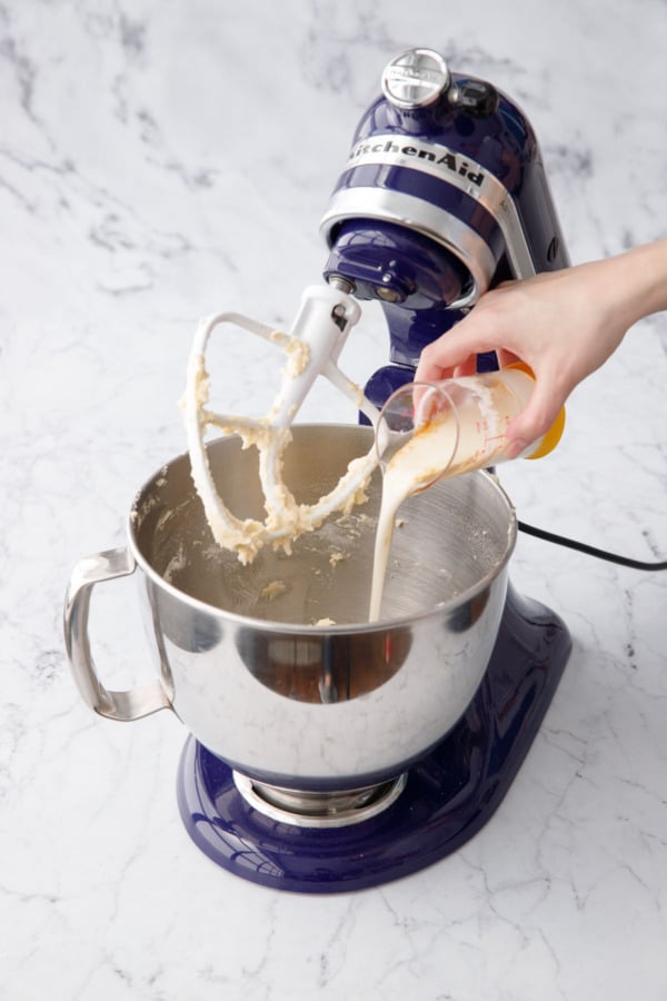 Pouring in buttermilk, oil, and vanilla into mixing bowl with cake batter.