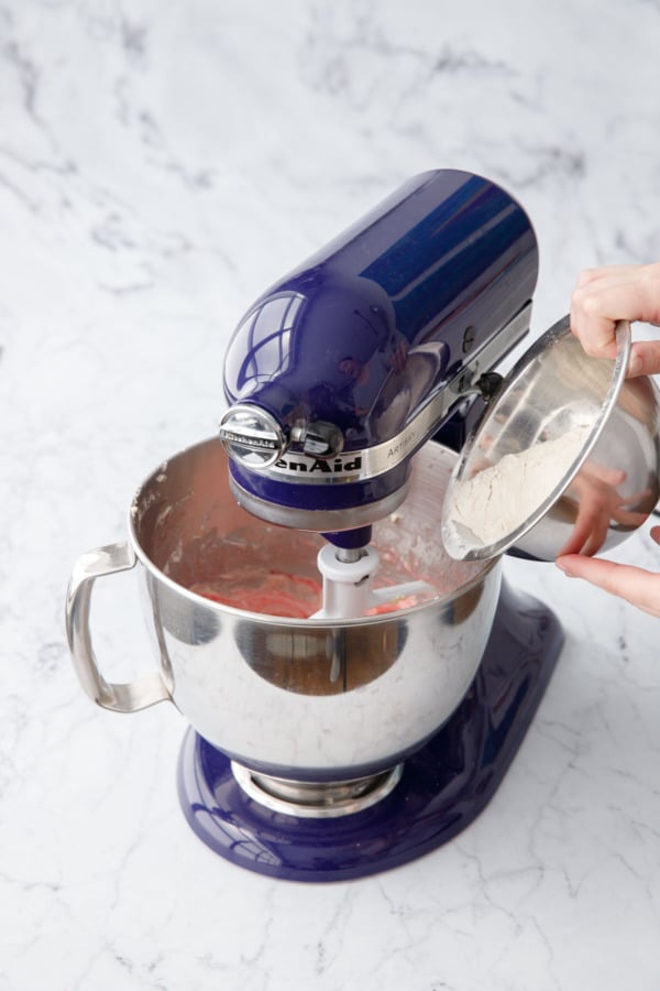 Pouring remaining flour into mixing bowl with pink-tinted cake batter.