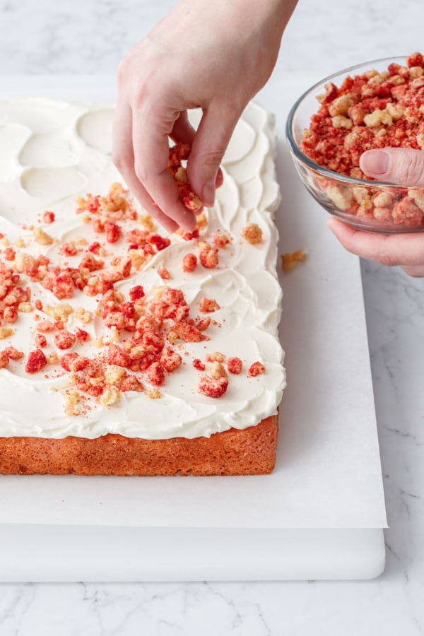 Sprinkling strawberry shortcake crunch topping mixture over top of buttercream-frosted strawberry cake.