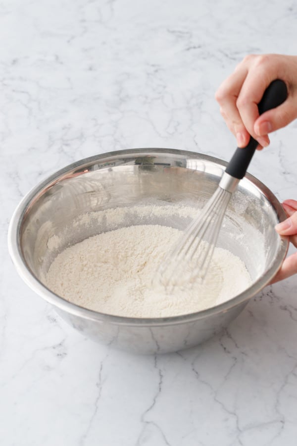Whisking flour and other dry ingredients together in a metal mixing bowl.