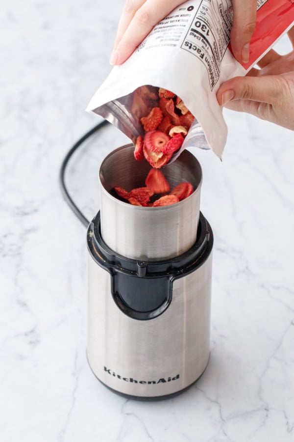 Pouring freeze dried strawberry slices into a coffee grinder.