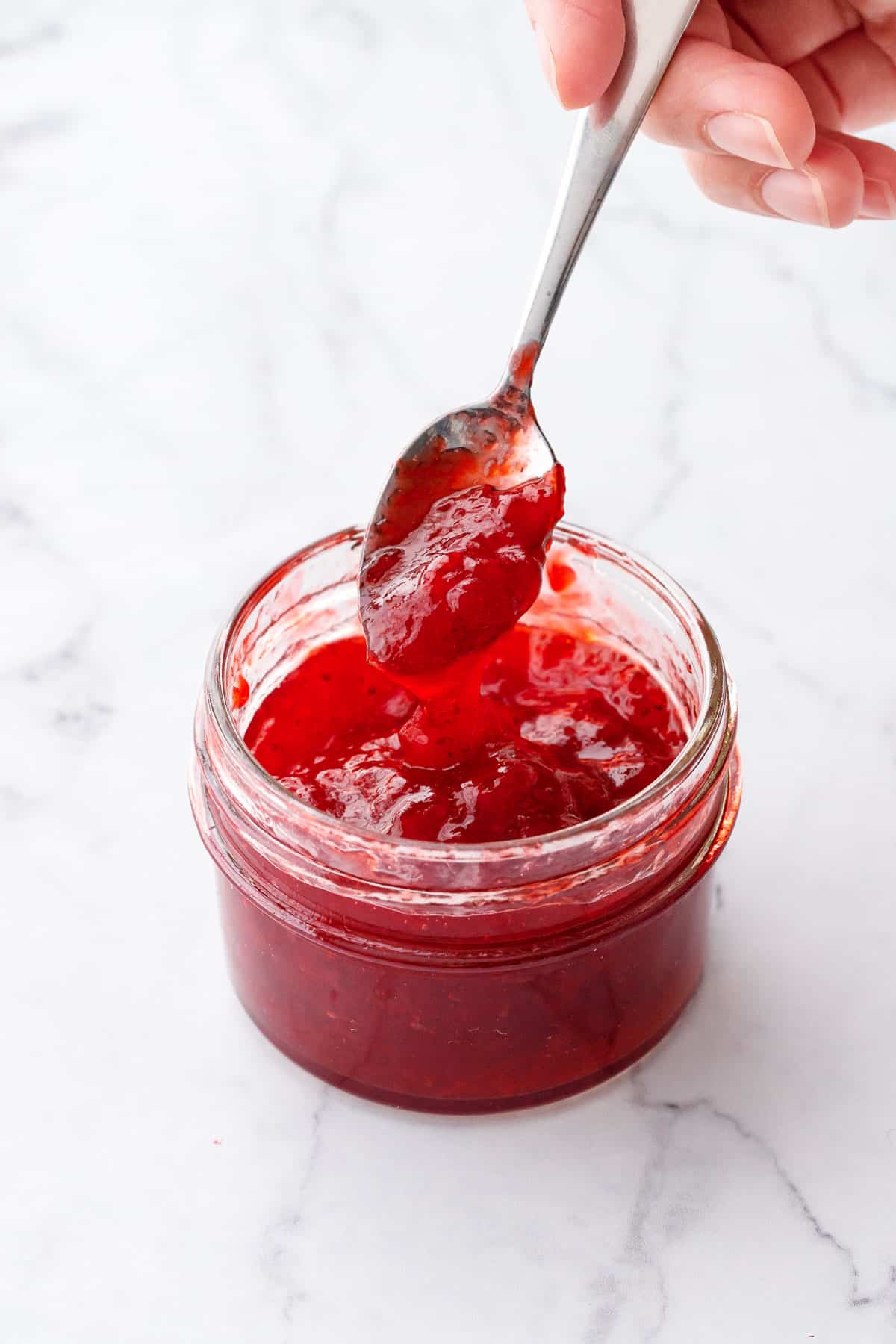 Spoonful of traditional strawberry jam made with regular pectin, showing the bright red color and smooth, jammy texture.