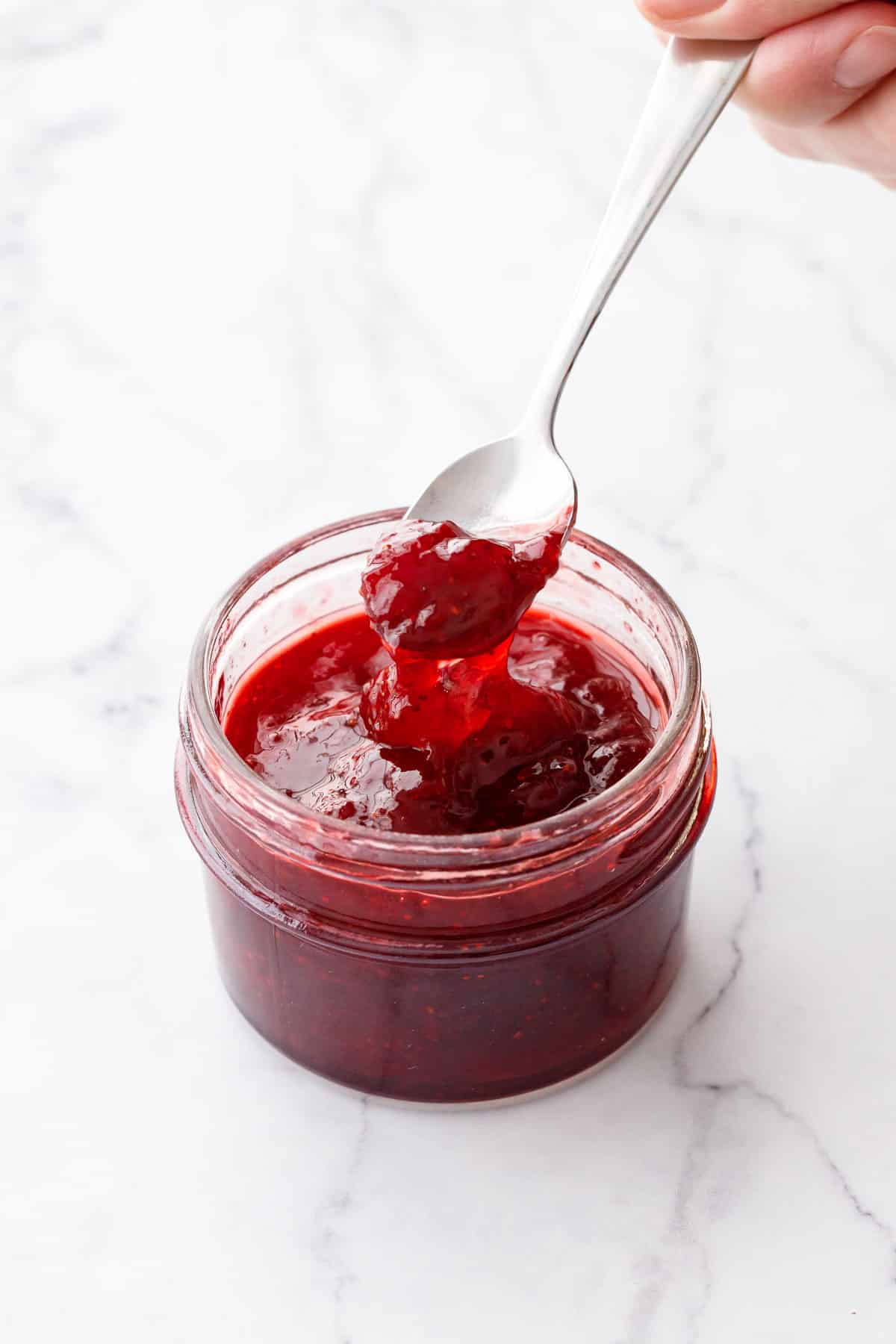 Spoonful of old-fashioned strawberry jam made without pectin, showing the thick and sticky texture and deep red color.