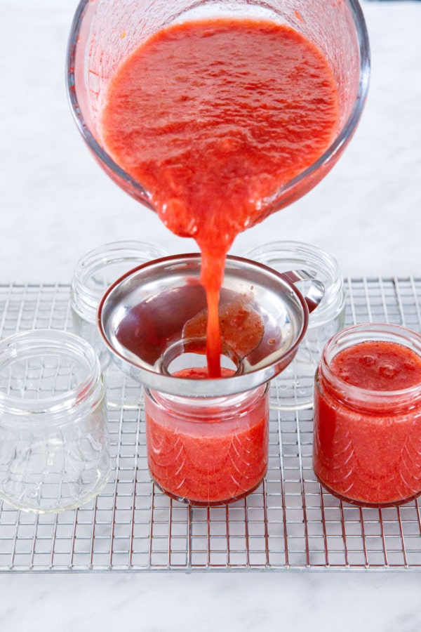 Pouring cooked Guava Strawberry Jam into canning jars with a stainless jar funnel.