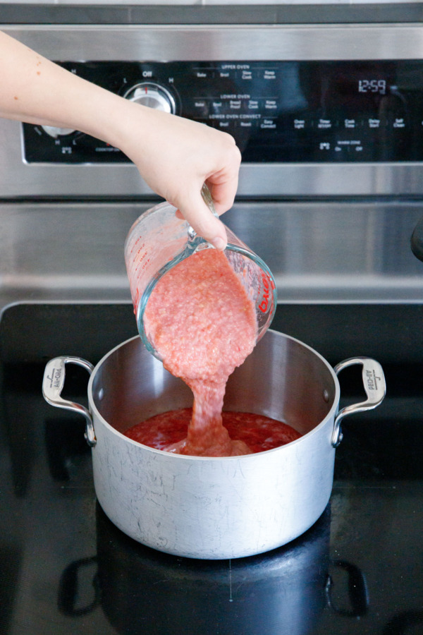 Pouring guava puree into saucepan along with mashed strawberry.