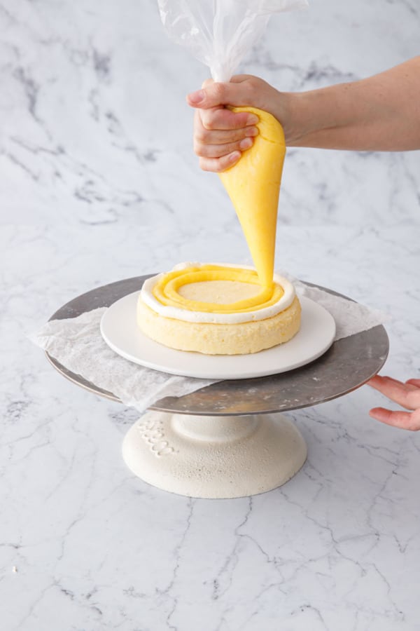 Piping lemon curd onto cake layers inside a ring of buttercream.