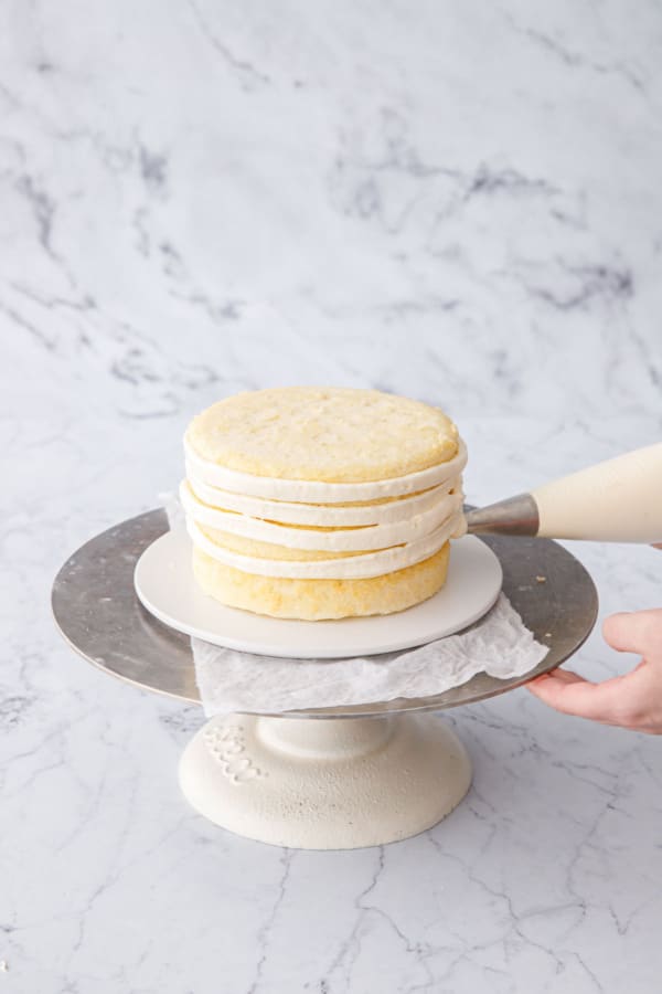 Piping a thin layer of buttercream on the outside of assembled layer cake for the crumb coat.