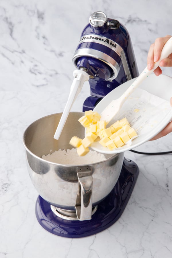 Adding cubes of cool room temperature butter to mixing bowl with dry ingredients.