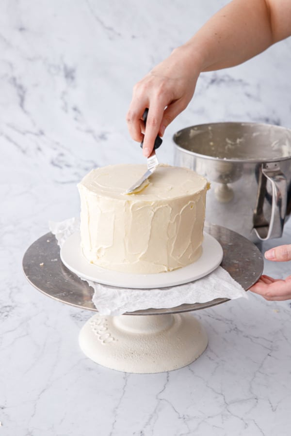 Using an offset spatula to spread the frosting evenly over the top and sides of cake.