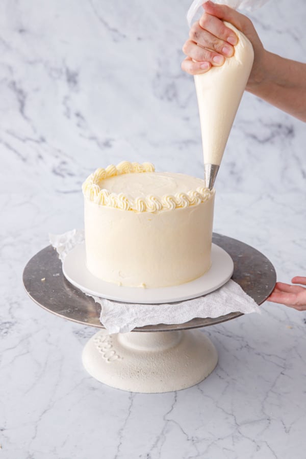Piping a decorative border onto the final frosted lemon layer cake.