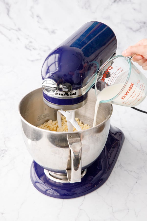 Pouring half of milk and lemon juice into mixing bowl with butter-coated flour.
