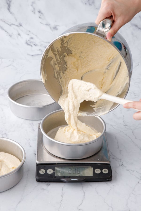 Pouring the cake batter into a 6-inch aluminum cake pan set on a kitchen scale.