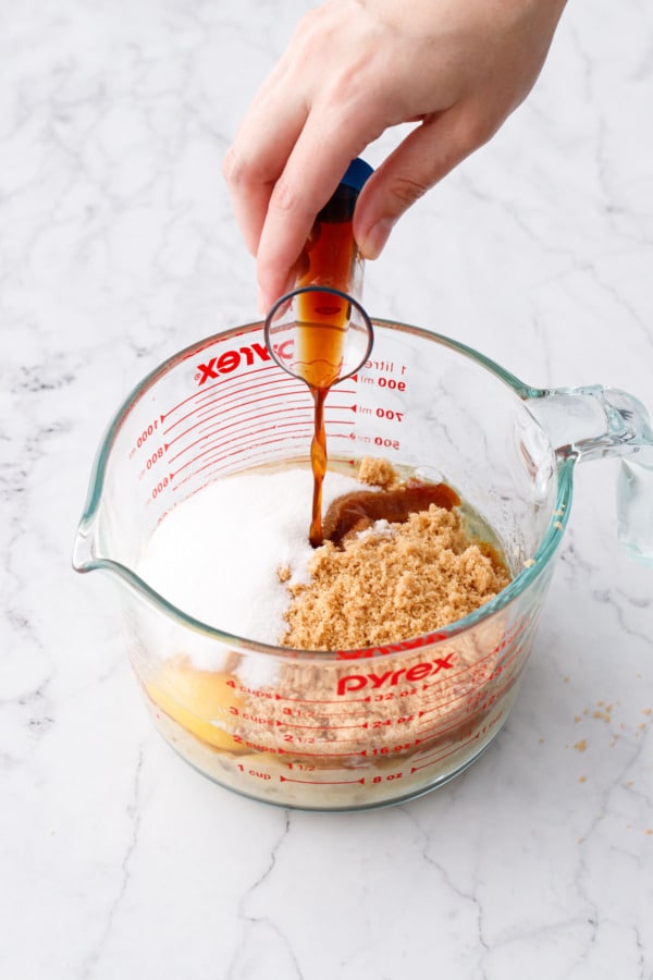 Pouring vanilla extract into measuring container with other wet ingredients and sugars.