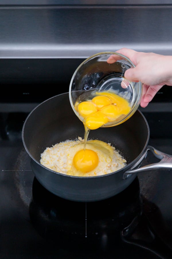 Adding egg and egg yolks to saucepan along with lemon zest and sugar.