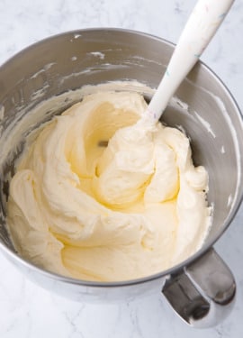 Bowl of Swiss Meringue Buttercream in a metal mixing bowl with white sprinkle spatula.