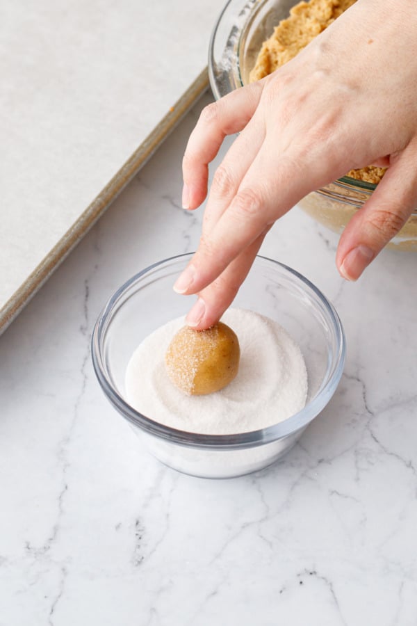 Rolling a ball of peanut butter cookie dough in granulated sugar to coat.