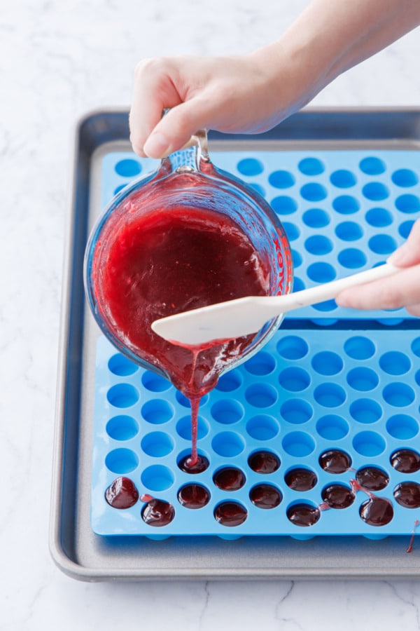 Pouring raspberry pectin gummy mixture into round silicone molds.