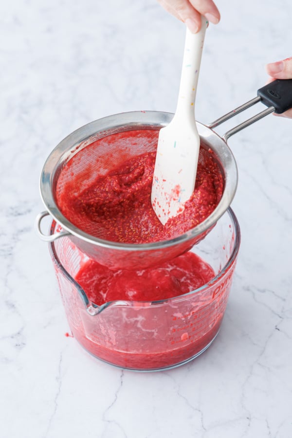 Pressing raspberry puree through a fine mesh sieve to remove seeds.