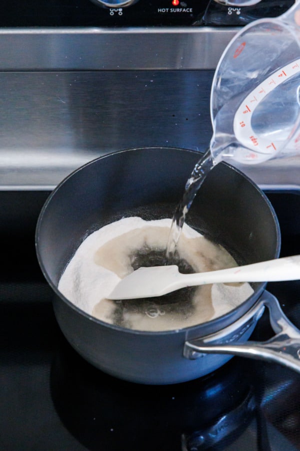 Pouring water into a small saucepan with pectin and baking soda.