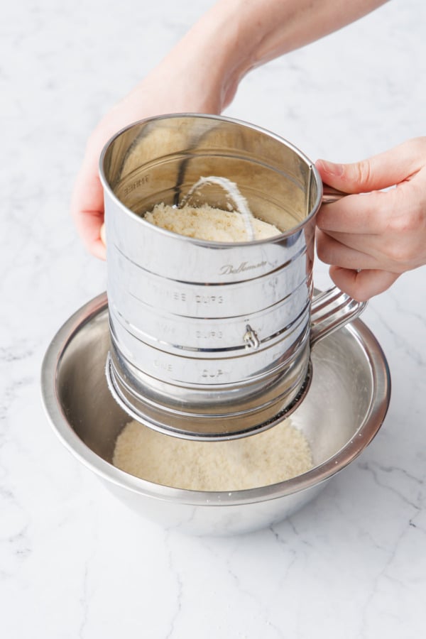 Sifting almond flour into a metal mixing bowl.