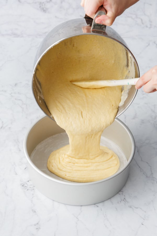 Pouring batter into a buttered 9-inch round cheesecake pan lined with parchment paper.